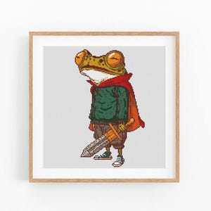 May include: A framed pixel art print featuring a frog dressed as a medieval knight. The frog wears a green sweater, red cape, and carries a sword. The artwork has a whimsical, cartoonish style, with a light gray background.