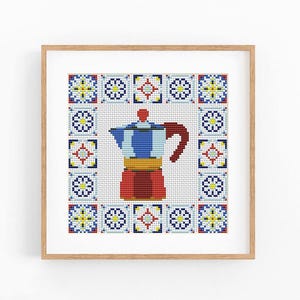 May include: A framed cross-stitch embroidery featuring a central moka pot in blue, red, and yellow, surrounded by a decorative border of repeating geometric tile patterns in blue, red, yellow, and white on a white fabric background.