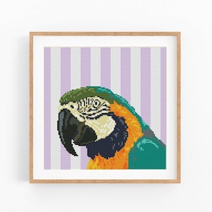Könnte beinhalten: Ein gerahmtes Kreuzstich-Kunstwerk mit einem lebendigen blau-goldenen Ara-Papagei. Der Kopf des Vogels ist mit Grün, Schwarz und Weiß detailliert, vor einem gestreiften lila-weißen Hintergrund. Das Kunstwerk befindet sich in einem Holzrahmen.