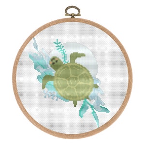 May include: A cross-stitch embroidery hoop with a green turtle swimming in blue water with white and green floral accents.