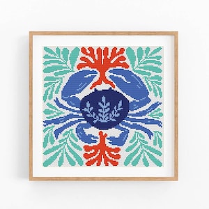 May include: A cross-stitch pattern featuring a blue crab surrounded by red coral and green leaves. The design is framed in a natural wood frame.