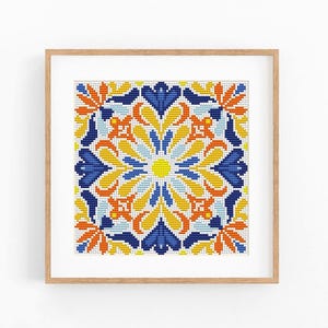 May include: A square cross-stitch embroidery featuring a symmetrical geometric pattern in shades of deep blue, bright yellow, and vibrant orange, encased in a light-toned wooden frame with a white mat border, displaying intricate needlework detail.