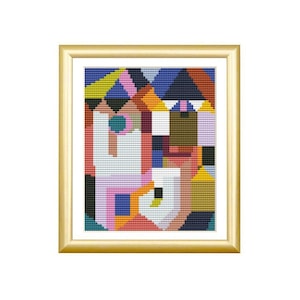 May include: A framed cross-stitch embroidery featuring a geometric abstract pattern composed of small, square stitches in vibrant colors including yellow, pink, blue, orange, brown, and white, enclosed within a metallic gold-toned frame.