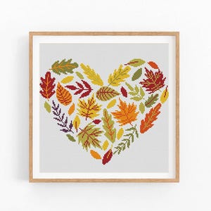 May include: Cross stitch pattern of a heart made of colourful autumn leaves. The leaves are in shades of red, orange, yellow, and green. The heart is surrounded by a white background.