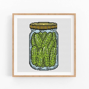 May include: A glass jar filled with green pickles. The jar has a yellow lid and is sitting on a white background.