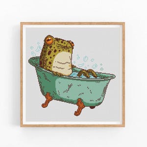 Puede incluir: Una rana verde se sienta en una bañera con burbujas. La rana es verde con manchas marrones y tiene una gran sonrisa. La bañera es verde y blanca.