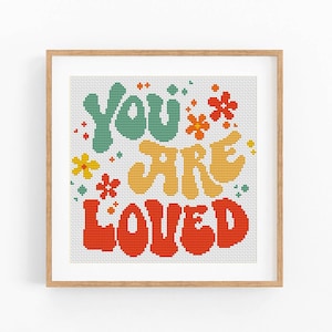 Może przedstawiać: Wzór do haftu krzyżykowego z napisem "You are Loved" w retro czcionce z kolorowymi kwiatami. Litery są w odcieniach zieleni, żółci i czerwieni.