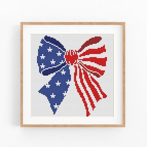 May include: Cross-stitch artwork of a patriotic bow in a wooden frame. The bow features a blue section with white stars and a red and white striped section, evoking the American flag. The artwork is displayed on a white background.