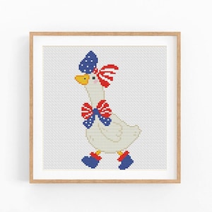May include: A framed cross-stitch of a white goose decorated with patriotic red, white, and blue accents. The goose wears a bow tie, a hat, and shoes in the colors of the American flag. The artwork is displayed in a light brown wooden frame.
