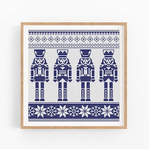 May include: A framed cross-stitch pattern featuring four blue nutcracker figures against a white background with a blue and white geometric border.