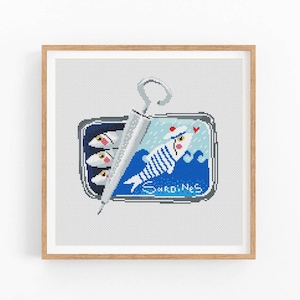 Può includere: Uno schema di punto croce che rappresenta una scatoletta di sardine con una sardina a strisce che indossa un cappello da marinaio e un ombrello che sporge dalla scatoletta. Il testo "Sardines" è stampato sulla scatoletta.