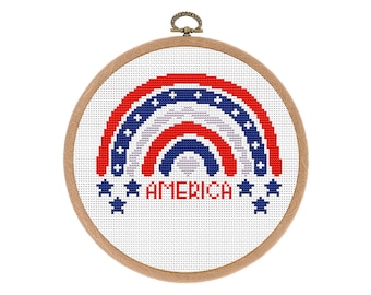 May include: A white embroidery hoop with a red, white, and blue rainbow design and the word "AMERICA" in blue lettering. The rainbow is made up of three arcs, each with a different pattern of stars.