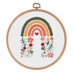 Peut inclure: Un cerceau de broderie avec un arc-en-ciel brodé, un cœur au centre de l'arc-en-ciel et des motifs floraux de chaque côté.