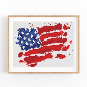 May include: A framed cross-stitch design of an American flag with a watercolor effect. The flag is red, white, and blue and is slightly faded and distressed. The design is framed in a natural wood frame.