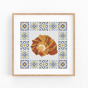 May include: A square cross-stitch embroidery featuring a central brown and tan seashell motif surrounded by a decorative border of repeating blue, yellow, and white geometric tile patterns, all encased in a light-coloured wooden frame.