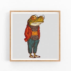 May include: A green frog wearing a red jacket, a brown sweater, blue jeans, and glasses. The frog is standing on a white background.