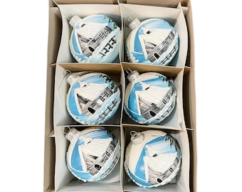Op de afbeelding: Set van zes witte glazen kerstballen met blauwe en witte geschilderde winterse taferelen. Elke bal heeft een huis met een besneeuwd dak en een zeilboot op de voorgrond.