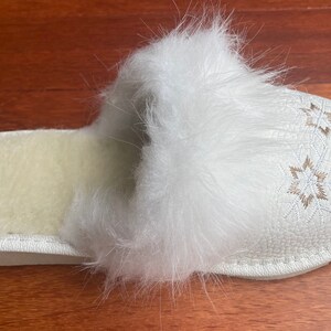 May include: White faux fur slipper with a white leather sole and embroidered snowflake designs.
