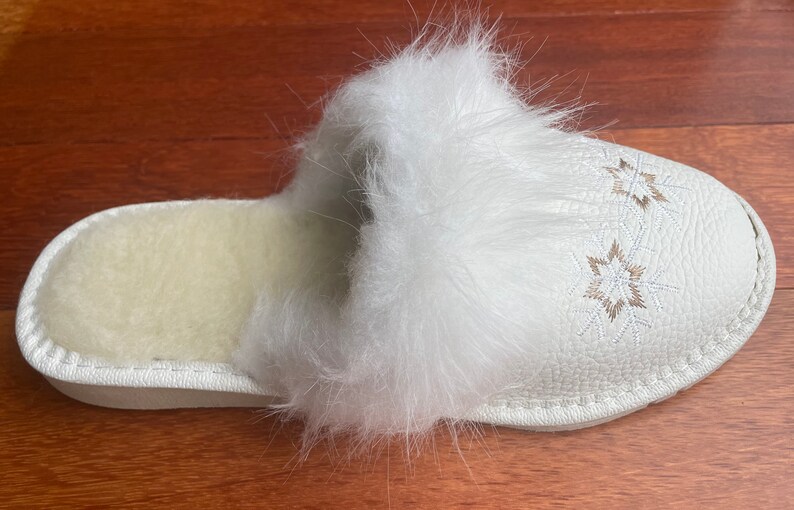 May include: White faux fur slipper with a white leather sole and embroidered snowflake designs.