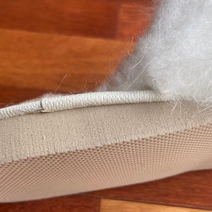 May include: Close-up of the bottom of a white fluffy slipper with a beige sole. The sole has a textured pattern.