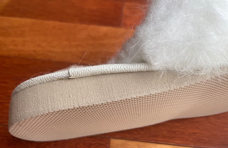 May include: Close-up of the bottom of a white fluffy slipper with a beige sole. The sole has a textured pattern.