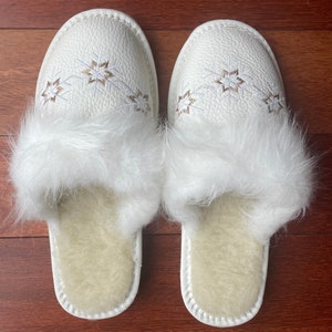 May include: White faux fur lined slippers with a white leather upper and embroidered snowflake design.
