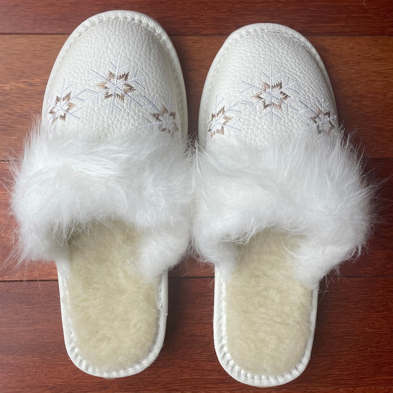 May include: White faux fur lined slippers with a white leather upper and embroidered snowflake design.