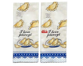 May include: Two white kitchen towels with blue trim and polka dots. Each towel features a drawing of pierogies and the text "I love pierogi". One towel also has the text "Made in Poland".