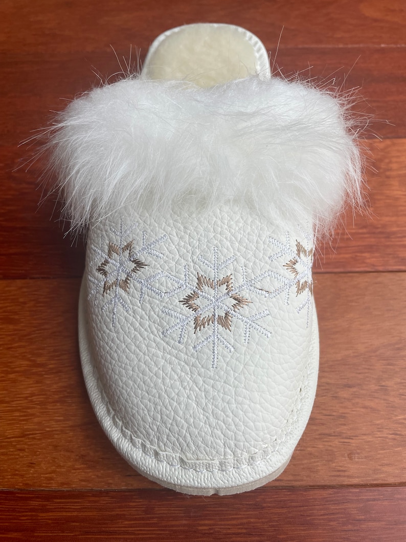 May include: White faux fur lined slippers with a white leather upper and embroidered snowflake design.