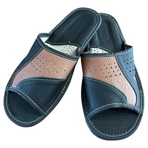 Op de afbeelding: Een paar zwarte leren slippers met bruine leren accenten en een geperforeerd ontwerp. De slippers hebben een gesloten teen en een open hiel.