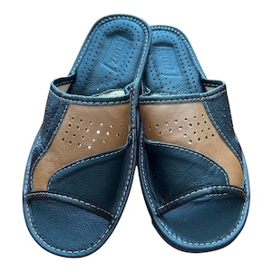 May include: A pair of open-toe slippers featuring a black and tan color-blocked design. The upper section is constructed from textured black and smooth tan leather panels with small ventilation perforations and visible white stitching.