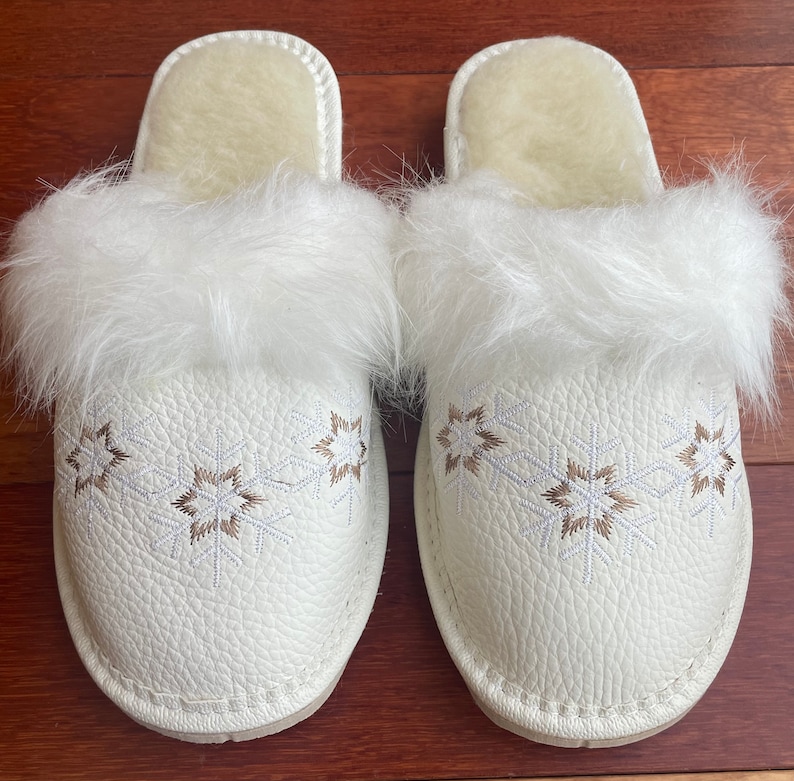 May include: White faux fur lined slippers with a snowflake pattern embroidered on the front.