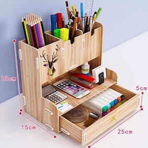 Könnte beinhalten: Ein hölzerner Schreibtisch-Organizer mit einer Schublade und Fächern für Stifte, Bleistifte und andere Büroartikel. Er verfügt über ein Hirsch-Ausschnitt-Design und misst 23 cm hoch, 15 cm breit und 25 cm lang.
