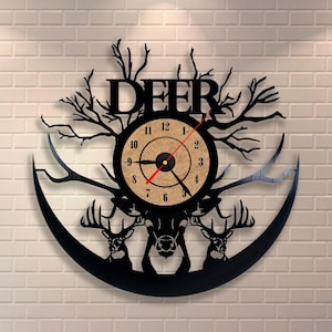 May include: Black vinyl record clock with a deer silhouette design. The clock face features a wood-grain background with black hands and Roman numeral markings. The word "DEER" is cut out of the vinyl record above the clock face.