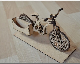 May include: A wooden model of a bicycle with a card holder attached to the back wheel. The model is made of light brown wood and has a detailed design.