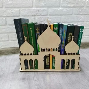 Könnte beinhalten: Ein Bücherregal aus Holz in Form einer Moschee mit zwei Minaretten. Das Bücherregal hält eine Reihe von Büchern mit Titeln in Arabisch und Russisch.