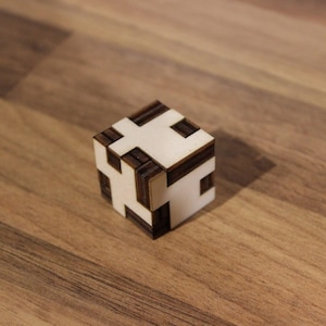 Op de afbeelding: Een houten kubuspuzzel met een wit en bruin geometrisch patroon. De kubus is gemaakt van meerdere stukken die in elkaar passen om een complex ontwerp te creëren.