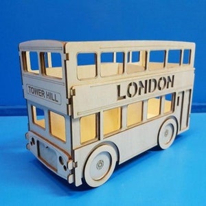 May include: A wooden model of a double-decker bus with the words "Tower Hill" and "LONDON" on the side. The bus is painted in a light wood color.