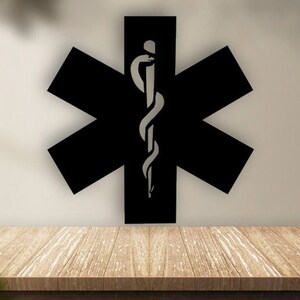 May include: A black and white medical symbol with a star of life and a caduceus. The symbol is on a white wall with a wooden surface in the foreground.