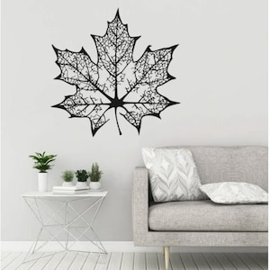 May include: Black and white silhouette of a maple leaf with intricate veins, displayed on a white wall above a gray sofa with a patterned pillow.