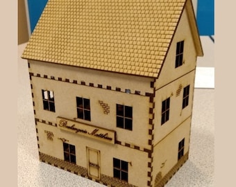May include: A two-story wooden model building with a brown roof and a sign that reads "Boulangerie Mathieu". The building has windows and a door. The model is made of laser-cut wood.
