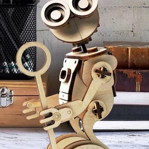 May include: A wooden robot toy with large round eyes and a stick in its hand. The robot is made of light brown wood and has a detailed design.