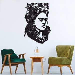 May include: Black metal wall art portrait of a woman with a floral crown and a bird on her shoulder. The artwork is mounted on a white wall, with green and wooden chairs and a small table in the foreground.