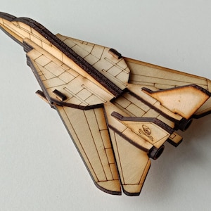 May include: A wooden model of a fighter jet with a brown and black paint scheme. The model is assembled and has a skull and crossbones design on the side.