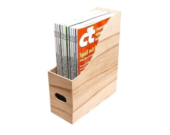 Peut inclure: Un porte-revues en bois avec une finition en bois de grain brun clair. Le porte-revues a un devant incliné et une poignée sur le côté. Il est rempli de magazines avec le titre "ct" et le texte "Spaß mit B" visible.