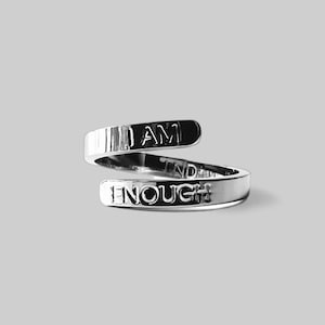 Peut inclure: Une bague en argent avec les mots "I AM ENOUGH" gravés dessus. La bague est torsadée et les mots sont visibles des deux côtés.