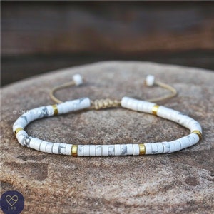 May include: White and gold beaded bracelet with a sliding knot closure. The bracelet is made with small, round white beads with gold accents.