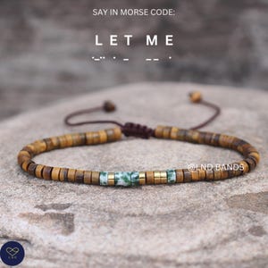 May include: A bracelet featuring brown and gold beads, with green and gold spacers. The text "SAY IN MORSE CODE: LET ME" is at the top. The bracelet is displayed on a stone surface. The brand name "@LND BANDS" is visible.