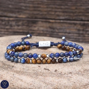 May include: A double-strand beaded bracelet featuring alternating blue lapis lazuli and brown tiger eye gemstone beads, accented with small silver-toned metal spacers. The bracelet includes a central rectangular silver-toned bead engraved with LND.