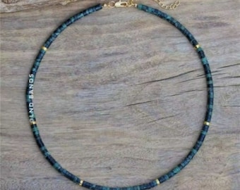 May include: A turquoise and black beaded necklace with gold accents. The necklace is made of small, square beads and has a gold clasp. The brand name "LND BANDS" is printed on the left side of the necklace.